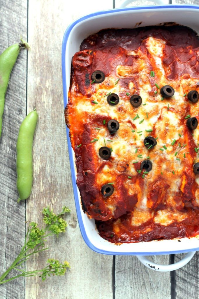 A top down look at pan of veggie enchiladas with broad beans and herbs in view.