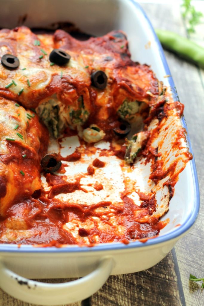 A pan of veggie enchiladas which have been cut open to reveal a goat cheese and vegetable filling.