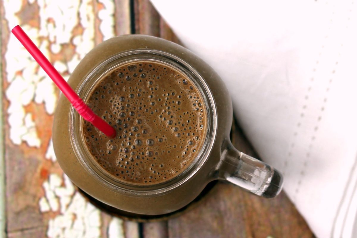 A banana, chocolate and chlorella smoothie with a pink straw, taken from the top down.