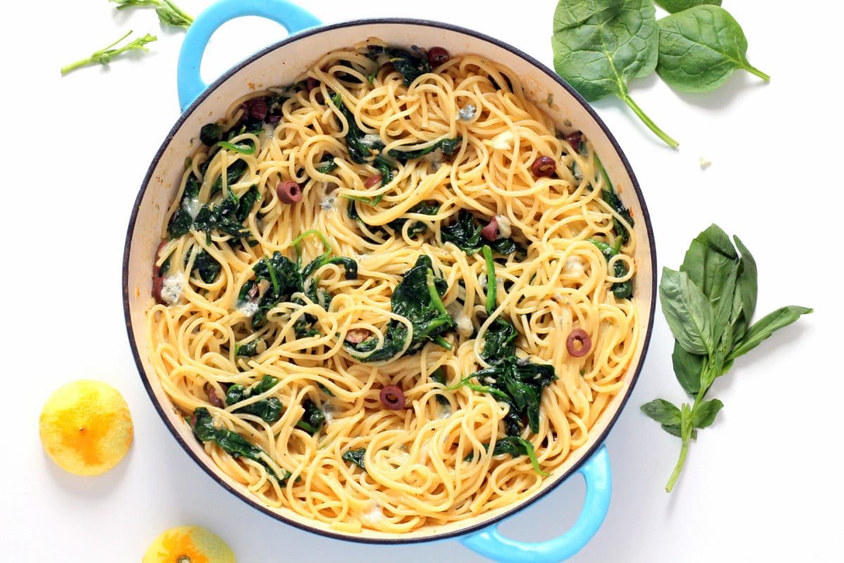 A top down view of a pan of spaghetti with spinach, gorgonzolas and lemons.