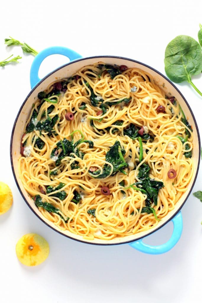 A top down view of a pan of spaghetti with spinach, gorgonzolas and lemons.