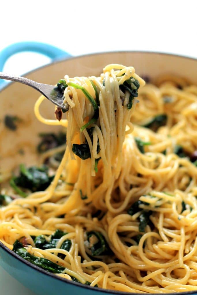 Apan of spaghetti with spinach, gorgonzolas and lemons, with a fork lifting some out.