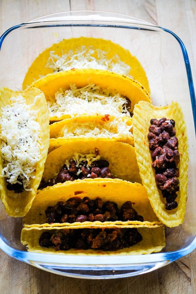 An image showing how to make baked tacos - taco shells are inside a dish, with beans and cheese stuffed inside.