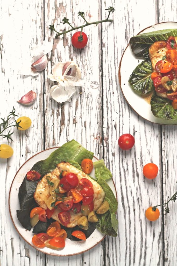 A flatlay showing two plates of bruschetta baked halloumi, with a scattering of cherry tomatoes and garlic around the plates
