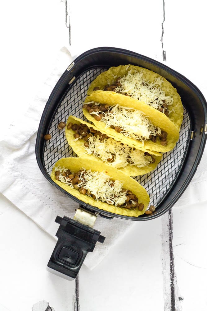 Cheese-topped tacos being prepared in an air fryer.