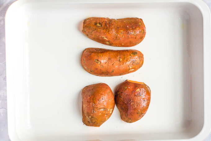 Sweet potatoes chopped in half and laying down on a baking sheet