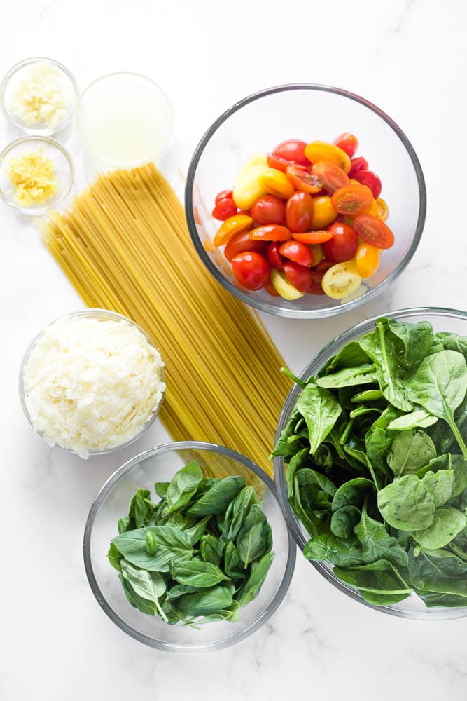 Bowls of prepped ingredients: spinach, basil, cheese, tomatoes, lemon juice and zest, dried spaghetti