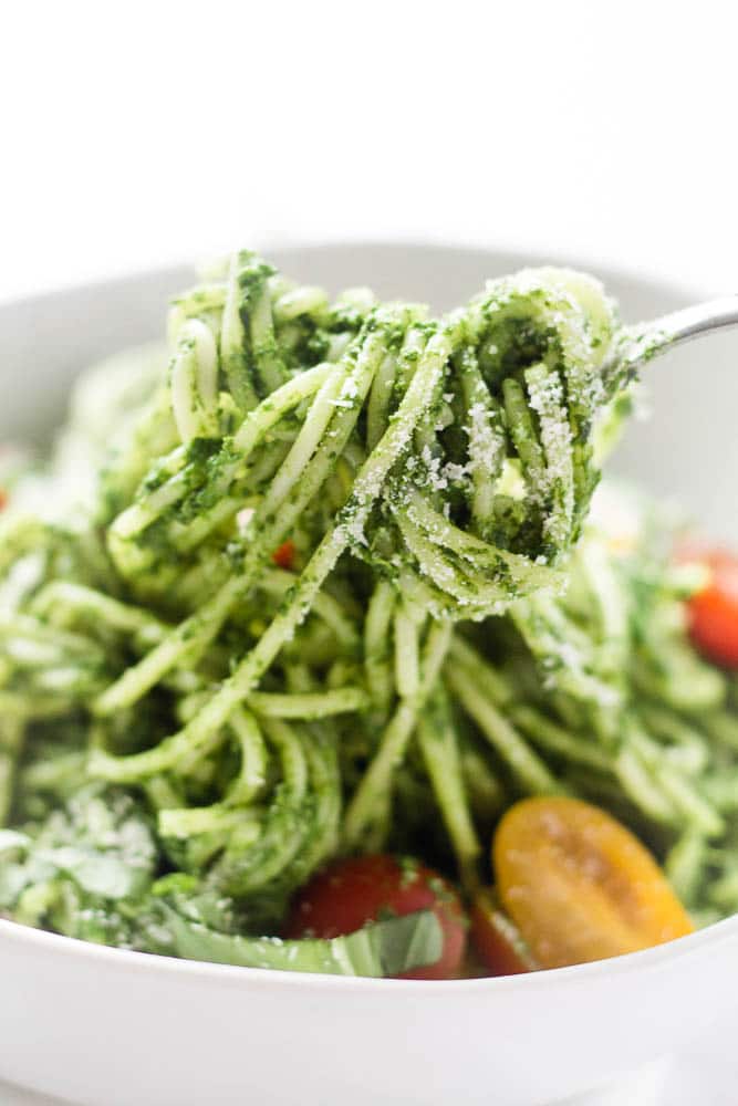 A bowl of green spaghetti with a fork lifting the spaghetti.