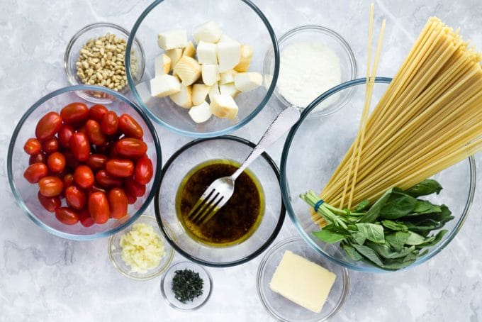 Ingredients for scamorza pasta with cherry tomatoes arranged in bowls. Dry pasta, scamorza cheese, pine nuts, parmesan, cherry tomatoes, garlic, thyme, butter and honey-balsamic glaze.