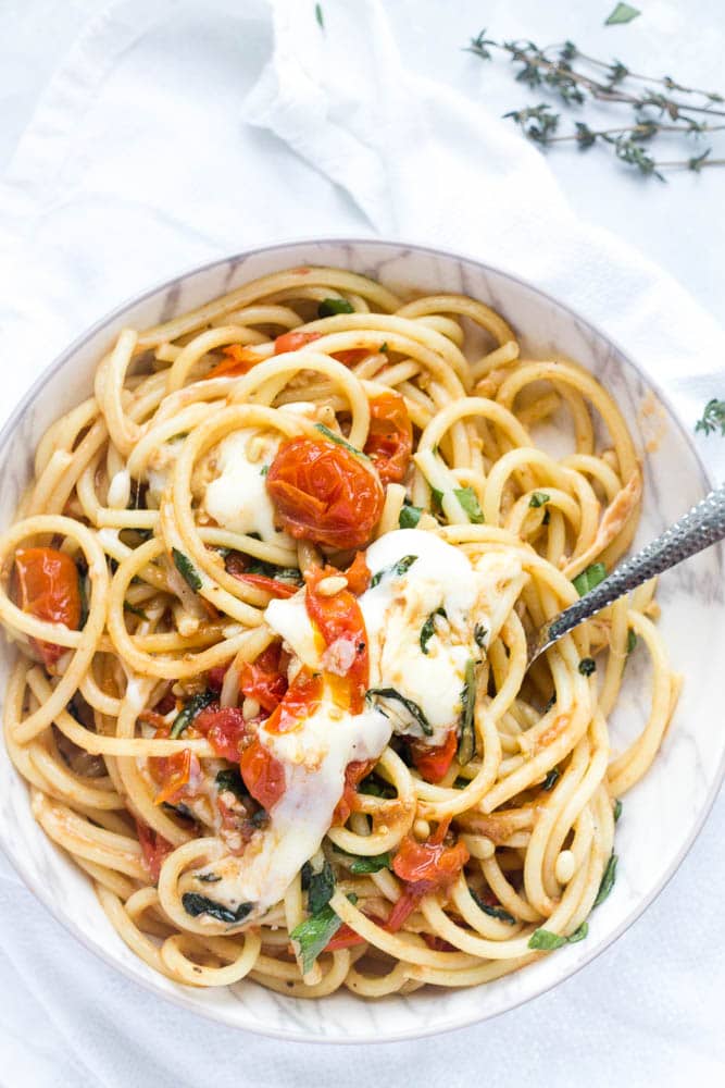 Close up of a single bowl of bucatini pasta with cherry tomatoes, scamorza cheese and pine nuts.