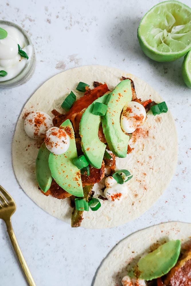 An open wrap showing halloumi fajitas made up, garnished with avocado and soured cream