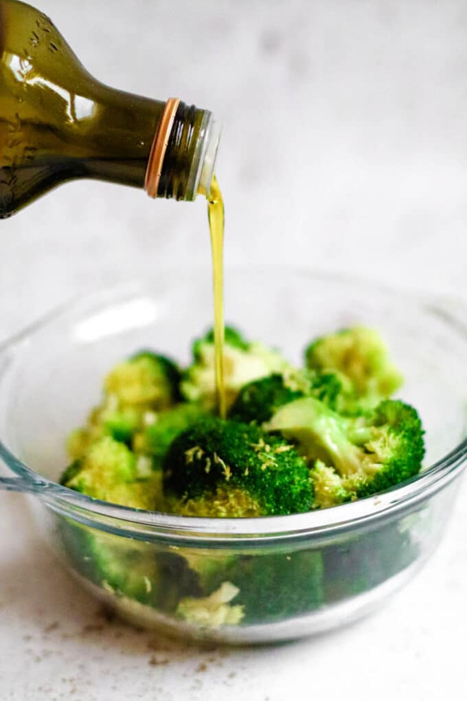Broccoli being drizzled with oil, in a bowl.