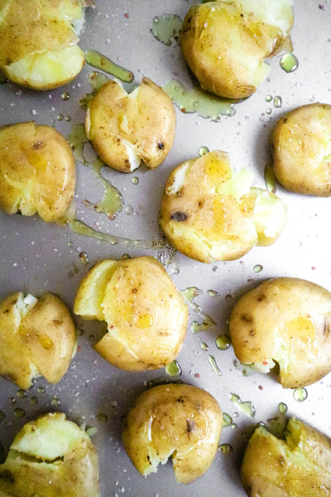 Smashed potatoes on a baking tray, drizzled with oil