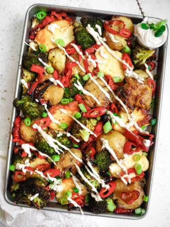 Top down view of sheet pan halloumi, broccoli and potatoes with garnishes and sauce.