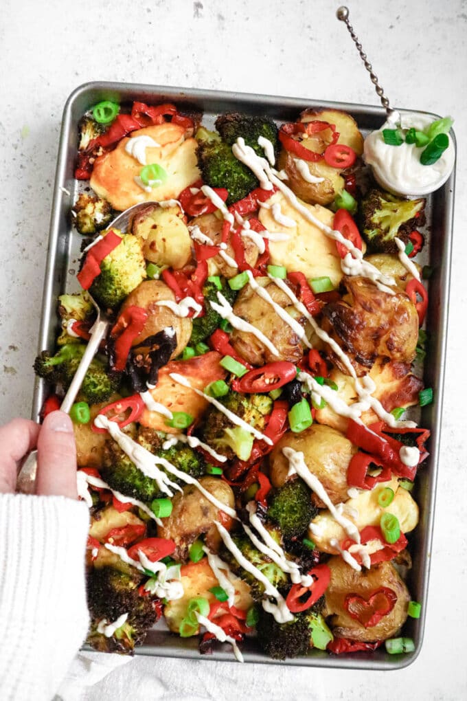 A large tray of roasted halloumi, potatoes and broccoli being served.