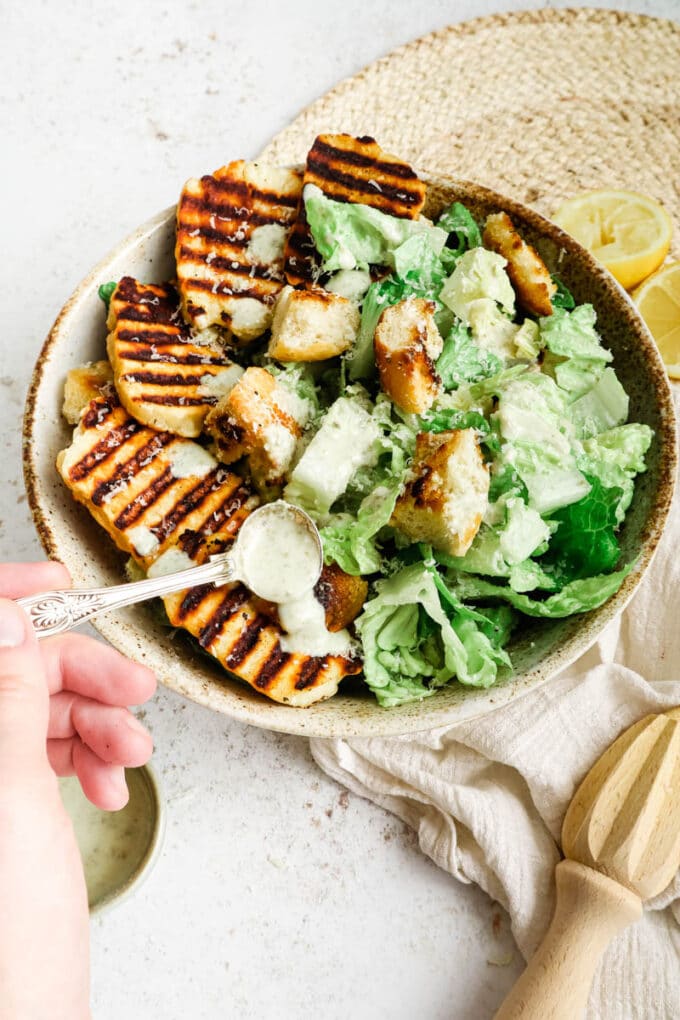 Halloumi caesar salad in a bowl with yogurt dressing being spooned over it