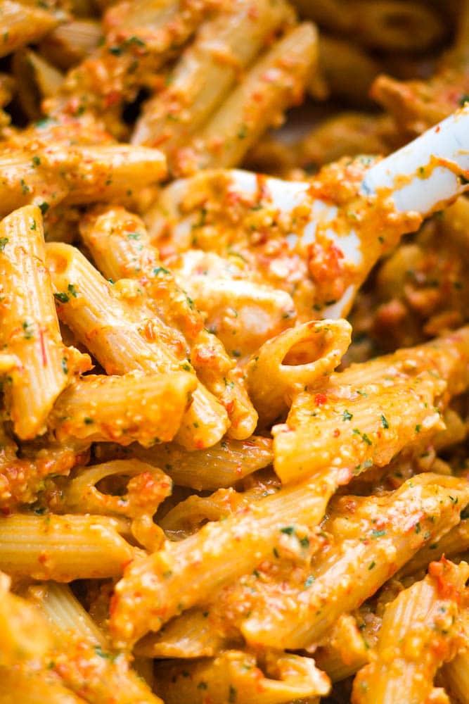 Red pepper pesto being mixed into pasta