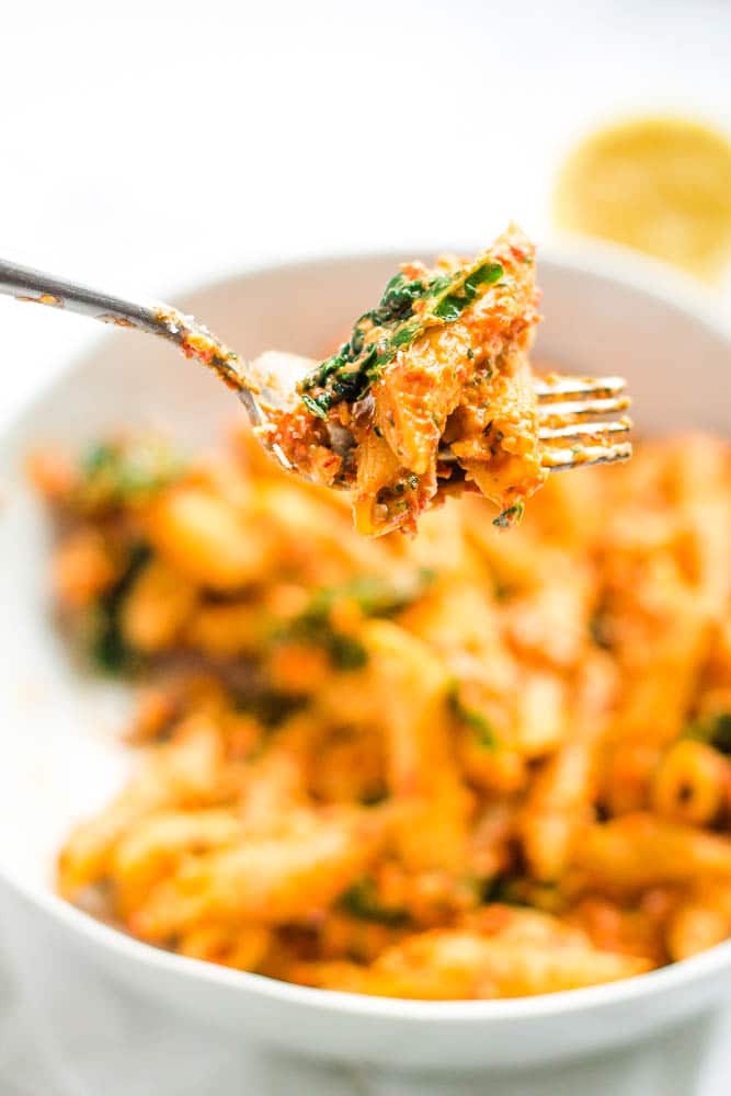 Close up of red pepper pesto penne on a fork
