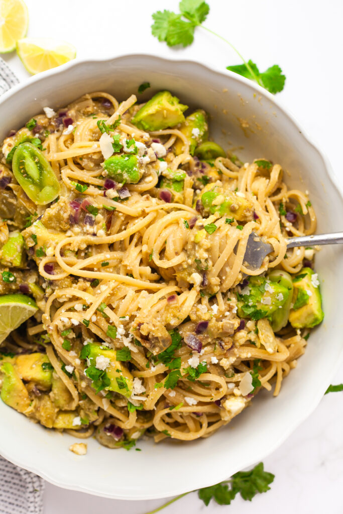 A top-down shot of the finished green tomato and avocado pasta garnished with fresh cilantro and lime
