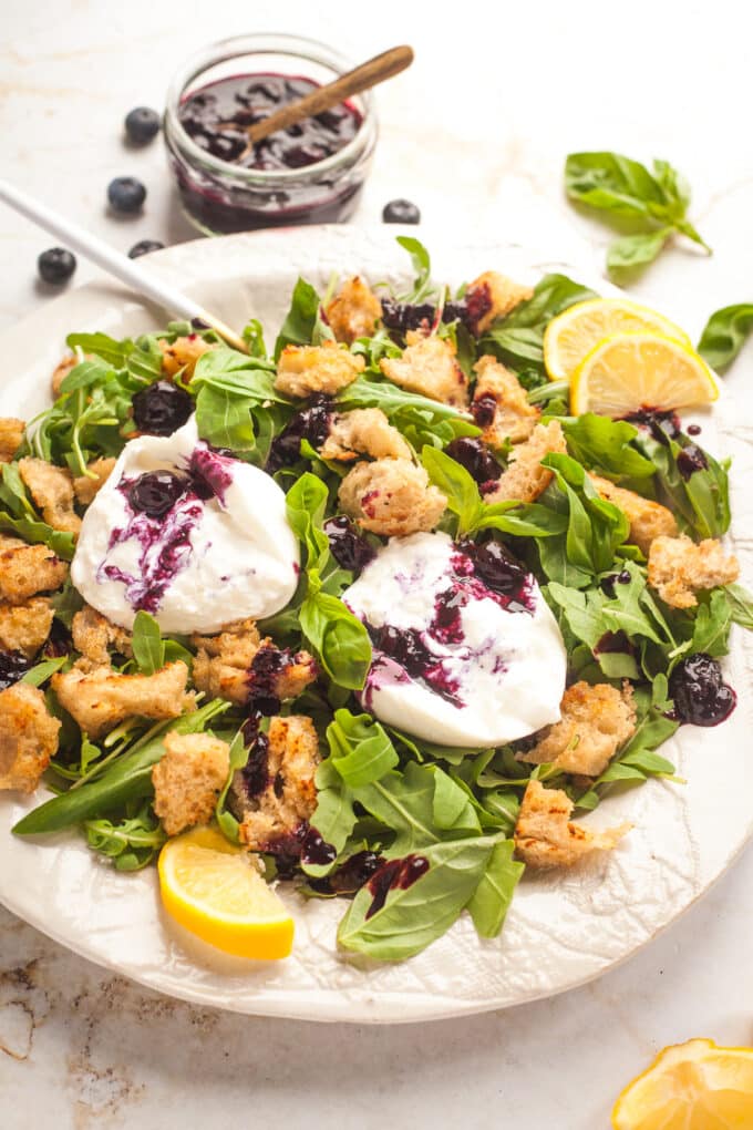 A plate of burrata and arugula salad with blueberry sauce and croutons.