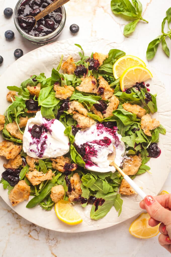 A plate of burrata and arugula salad with blueberry sauce and croutons.